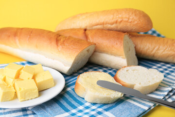 Whole and cut baguettes with fresh butter on yellow background, closeup