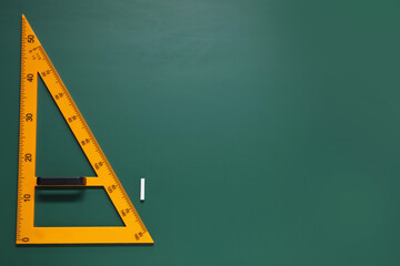 Yellow triangle and chalk on green chalkboard, flat lay. Space for text