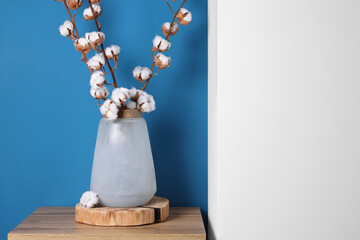 Cotton branches with fluffy flowers in vase on wooden table indoors. Space for text