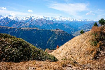 View of the vast mountains of Georgia in the Greater Caucasus. In the background are snow-capped mountains and in the foreground are hills of yellow and green grass