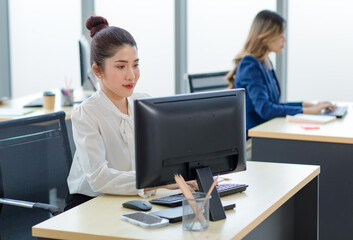 Obraz premium Portrait shot of Millennial Asian young professional successful female businesswoman secretary sitting smiling looking at camera working typing with computer keyboard in company office workstation.