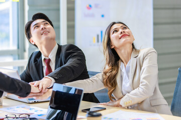 Millennial Asian young professional successful male female businessmen businesswomen in formal suit sitting smiling discussing holding hands showing unity together in company office working desk