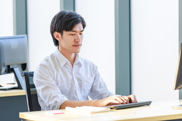 Portrait shot of Millennial Asian young professional successful male businessman sitting smiling looking at camera working typing with computer keyboard in company office workstation.