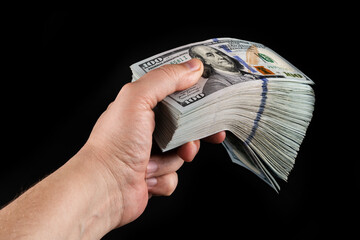 A man's hand holds a large stack of banknotes in denominations of 100 American dollars on a black...