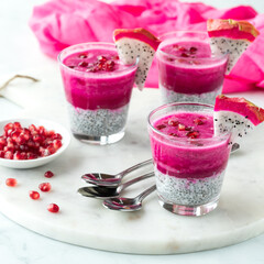 Three dragonfruit chia pudding parfaits, garnished with pomegranate arils.