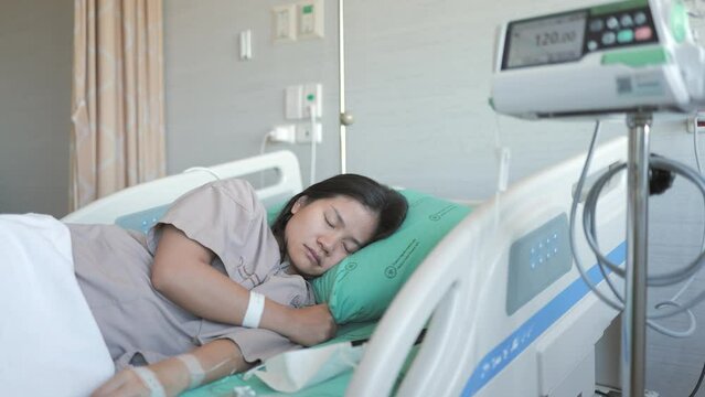 A woman patient on a hospital bed with a saline solution device injects NSS fluid from the IV bag.