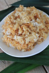 Indonesian food called ketan salak made of glutinous rice, coconut and palm sugar in an oval white plate on a table decorated with pandan leaves