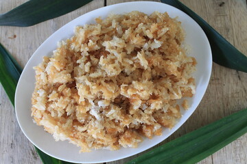 Indonesian food called ketan salak made of glutinous rice, coconut and palm sugar in an oval white plate on a table decorated with pandan leaves