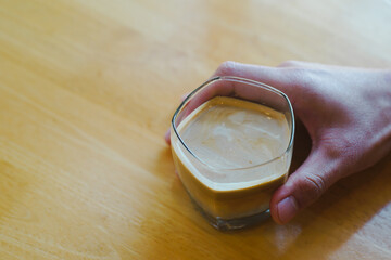 Hand holding glass of coffee on wooden table.