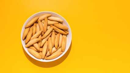 Top view of picos - bread sticks in the bowl on the yellow background with hard shadow and copy space