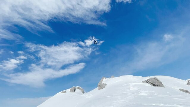 LOW ANGLE VIEW: Helicopter takes off a snowy mountain and flies towards valley. Flight transport for adventurous freeride heliskiing in picturesque and untouched wild mountains of spectacular Albania.