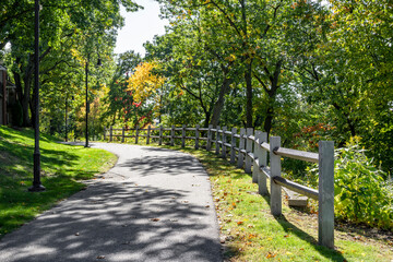Fototapeta premium Pedestrian path with a wooden fence on the alley with autumn trees and lighting lanterns