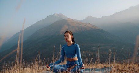 Athletic girl meditating during sunrise. Fit girl training in mountains, sitting in lotus yoga pose - healthy way of life, zen concept 