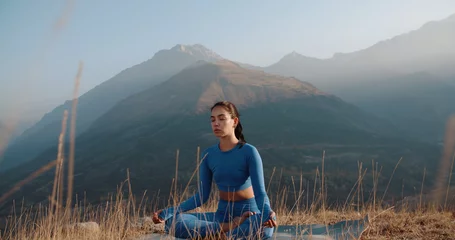 Tuinposter Athletic girl meditating during sunrise. Fit girl training in mountains, sitting in lotus yoga pose - healthy way of life, zen concept  © andreybiling