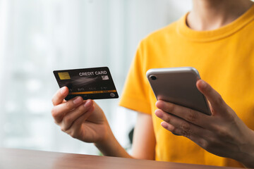 Woman hand holding credit card and using smartphone for paying products online via the Internet.