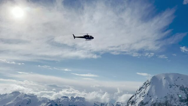 LOW ANGLE VIEW: Heliskiing helicopter flies over picturesque snowy mountain tops. Flight transport for adventurous freeride heliboarding in breath-taking and untouched mountains of spectacular Albania