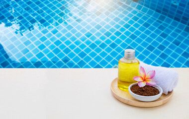 Coffee powder scrub and massage oil with Plumeria flower and towel on swimming pool edge, spa treatment concept, relaxing by the pool