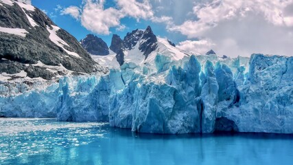 Closeup view of the textured surface of a glacier face, with jagged, snowcapped mountains in the background, in the Drygalski Fjord of South Georgia Island in the South Atlantic Ocean. © Cheryl Ramalho