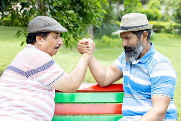 Playful senior indian men friends hand completion in arm wrestling in the summer park. Enjoying...