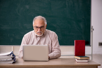 Old male teacher in front of green board