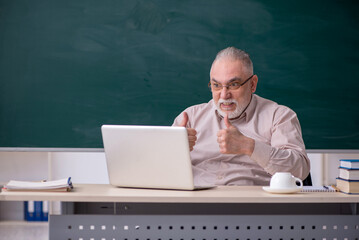 Old male teacher in front of blackboard