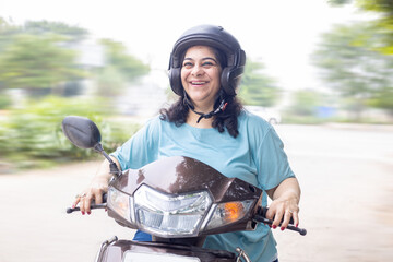 Happy senior indian woman wearing helmet riding motor scooter on road. Closeup