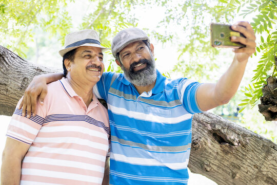 Happy senior indian men friends taking selfie picture with their smart phone outdoor at the summer park. Enjoying Retirement Life.