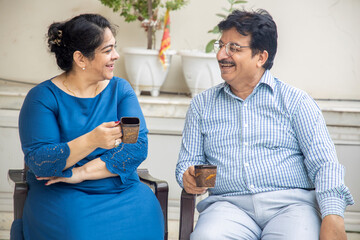 Happy indian middle age couple enjoying morning tea or coffee together and talking. Domestic or retirement life. - Powered by Adobe