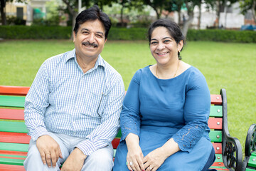 Happy indian senior couple sitting together at summer park.