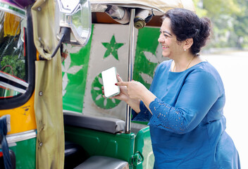 Happy mature indian woman doing online payment on her smart phone to rickshaw person.