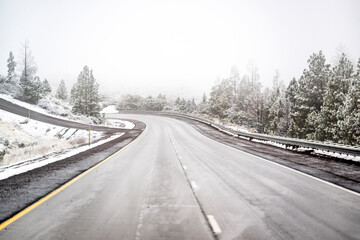 Snow-covered winter mountain winding road with snow white slopes dissolving into thick fog on a...