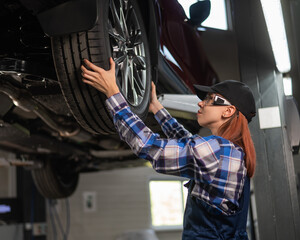 Female mechanic adjusting the tire of the car that is on the lift. A girl at a man's work.