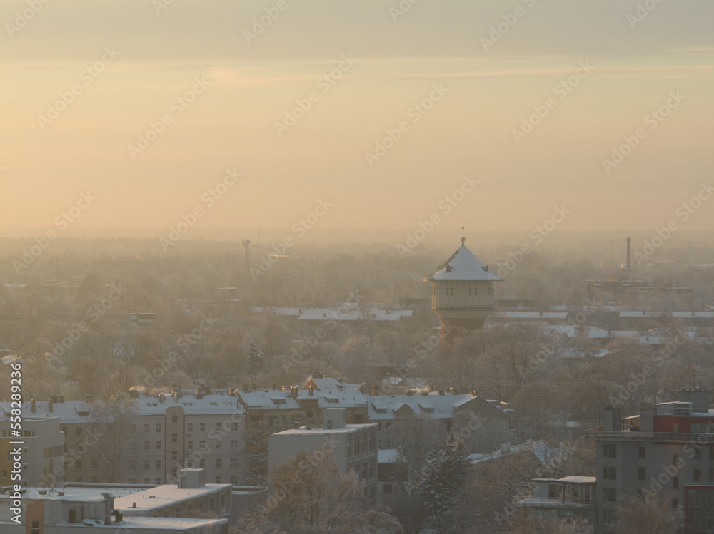 Poster a view of a city with a clock tower in the distance and snow on the ground and trees in the foregrou
