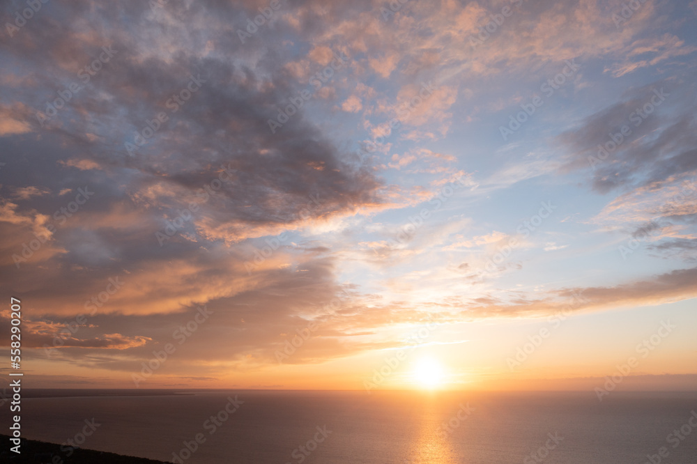 Poster the sun is setting over the ocean with a few clouds in the sky and a hill in the foreground with a g
