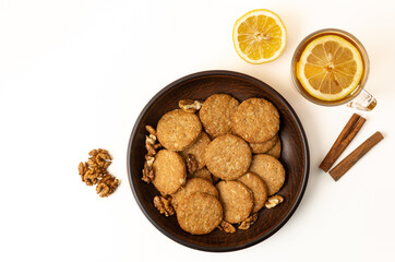 Cookies in a plate with nuts and a cup of tea with lemon on the table.