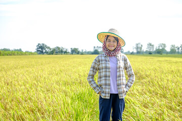 Naklejka na ściany i meble Asian female farmer wearing a striped shirt wearing a hat standing and posing with a smiling face at the rice field