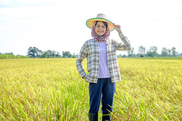 Naklejka na ściany i meble Asian female farmer wearing a striped shirt wearing a hat standing and posing with a smiling face at the rice field