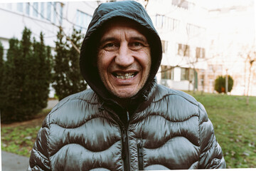 middle-aged man, in winter jacket with hood, smiles an ugly smile with crooked spoiled teeth  - obrazy, fototapety, plakaty