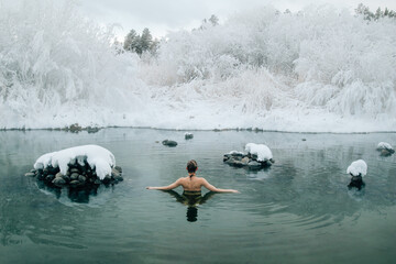 Young woman relaxing in hot springs during winter. Steam rises from the warm water, and snow surrounds the scene, creating a serene and tranquil atmosphere. She looks peaceful, enjoying the contrast b