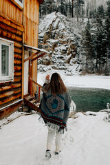 Young woman standing outdoors in winter by a mountain stream. She is dressed warmly and looks serene and contemplative. Snow-covered surroundings and flowing water create a calm, natural, and pictures