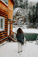 Young woman standing outdoors in winter by a mountain stream. She is dressed warmly and looks serene and contemplative. Snow-covered surroundings and flowing water create a calm, natural, and pictures