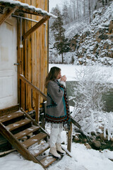 Young woman standing outdoors in winter by a mountain stream. She is dressed warmly and looks serene and contemplative. Snow-covered surroundings and flowing water create a calm, natural, and pictures