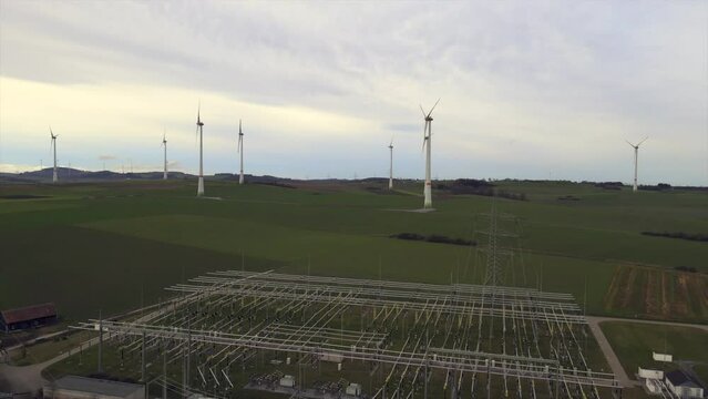 Aerial Backwards Shot of Critical Energy Production: Rotating Windmills on a Field with a Power Substation in the Foreground in Sauerland, Germany