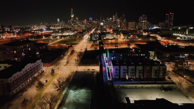 Train driving across the night lit Bronzeville cityscape in Chicago - Aerial view