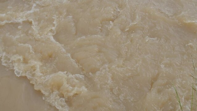 Flooded creek with brown water flowing at strong current daytime - summer