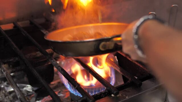 Skilled chef frying vegetables in pan on big flame stove, close up