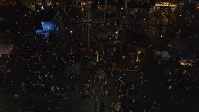 People gather to enjoy holiday night scene for Christmas tree lighting during snow flurries. Aerial truck shot.