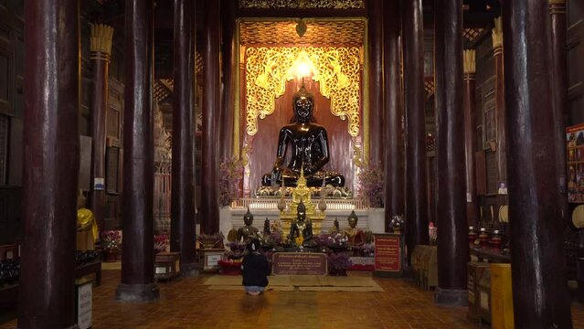 Woman Sitting Pray in Front of Black Buddha Statue In Buddist Temple