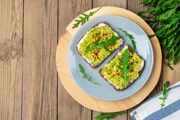 Set sandwiches for breakfast - slice of whole grain dark bread, cream cheese, guakomole, garnished with arugula, paprika on wooden table Top view Flat lay Healthy food concept Homemade