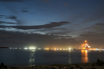 An industrial port filled with lights at night on the edge of the beach